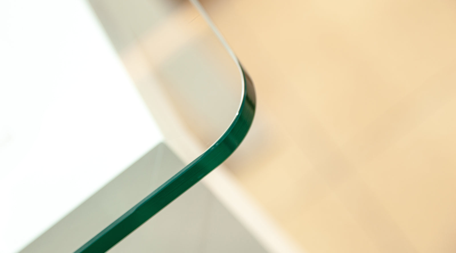 Close-up of a curved green-tinted glass tabletop corner with a blurred beige background.